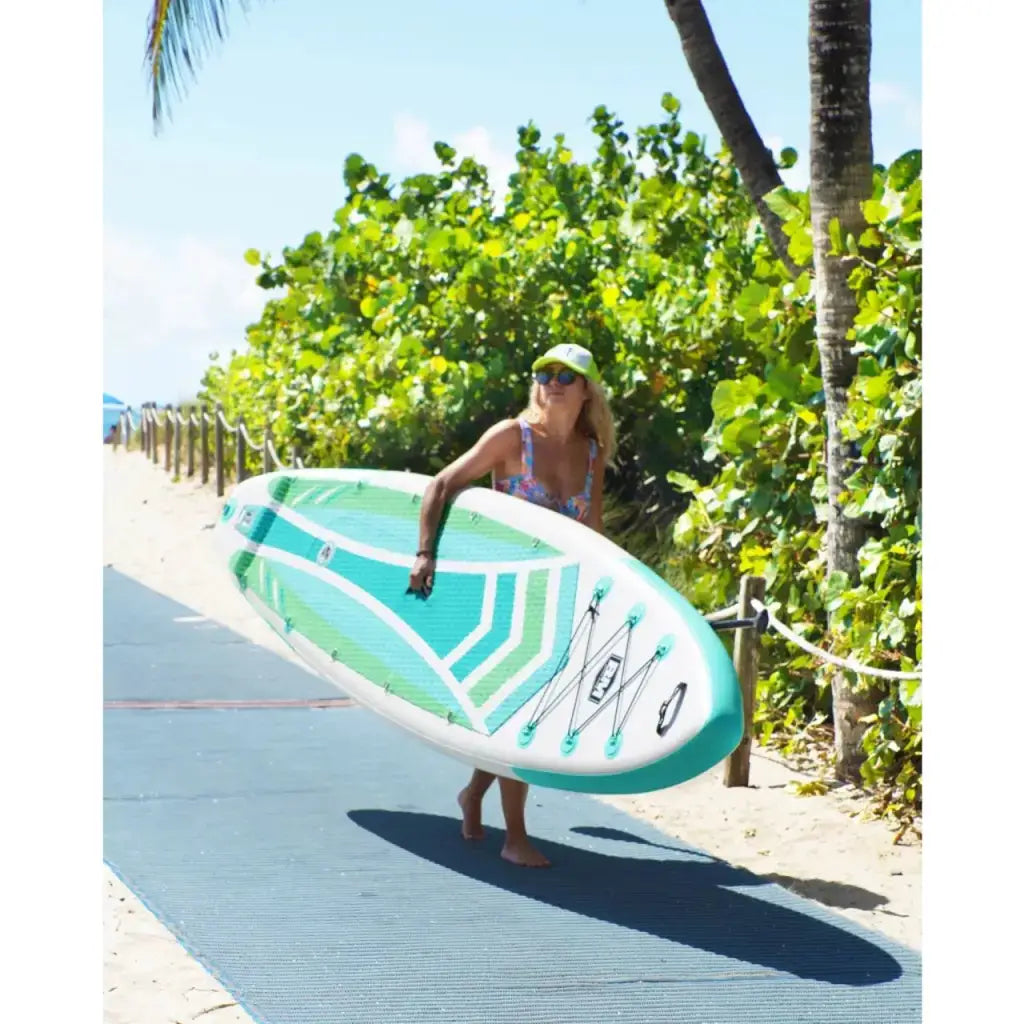 Woman carrying an 11’6 inflatable paddle board DUAL AIR down a beach path for a fun iSUP adventure